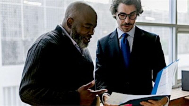 Two colleagues comparing printed documents while standing by a window