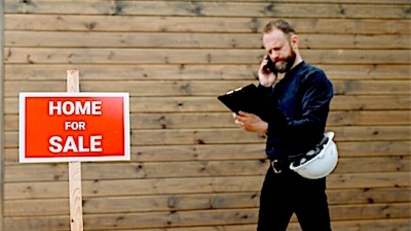 A real estate agent on the phone beside a home for sale sign